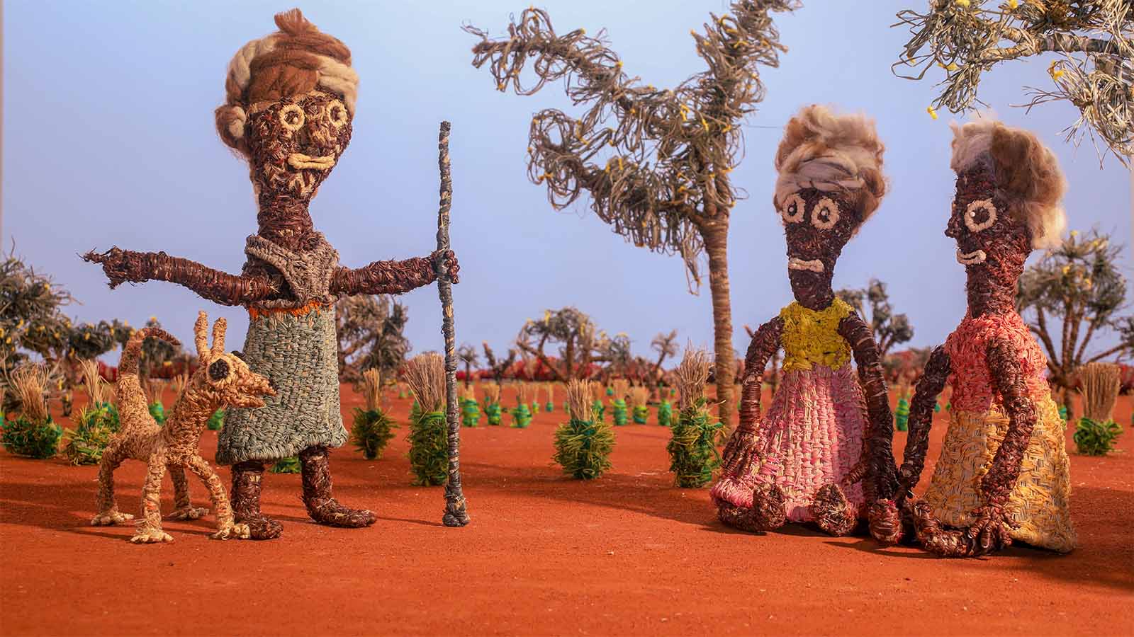 Three textured clay figures and a dog in a vibrant, surreal landscape with twisted trees and plants on red soil.