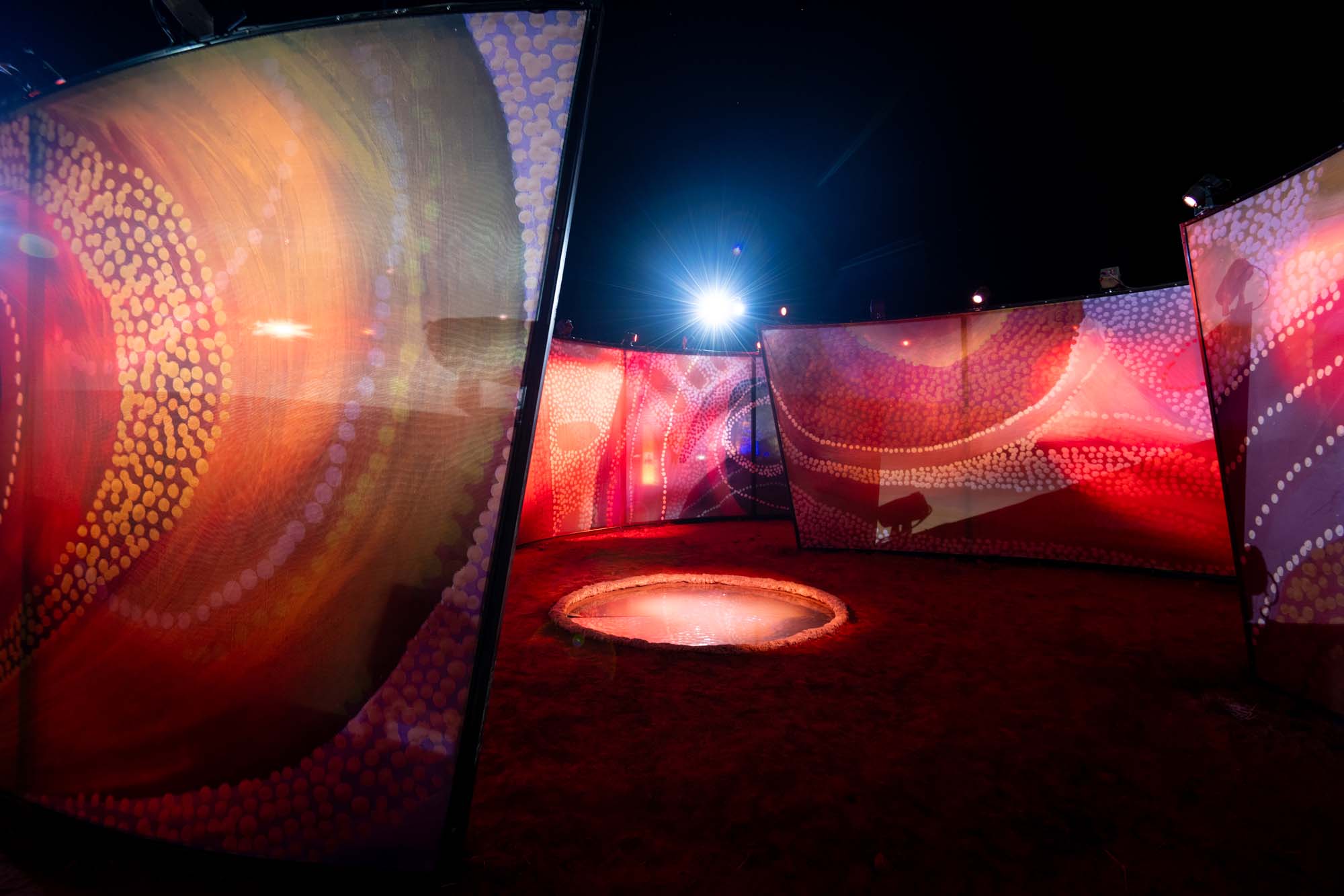 Abstract art installation with vibrant, curved panels in red and orange hues, illuminated by a bright light in the center.