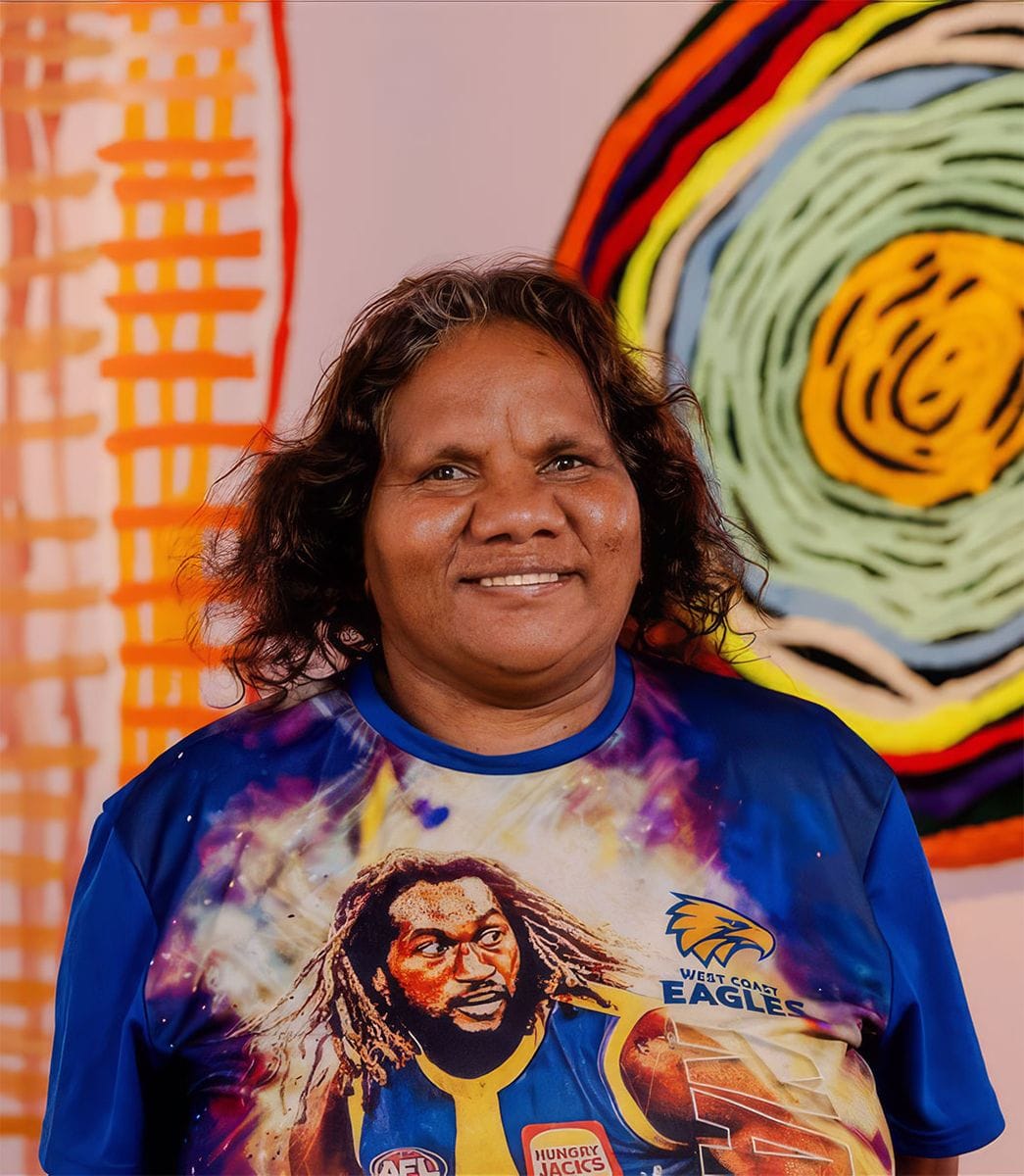 Smiling woman in a West Coast Eagles shirt stands in front of colorful artwork with circular and linear patterns.