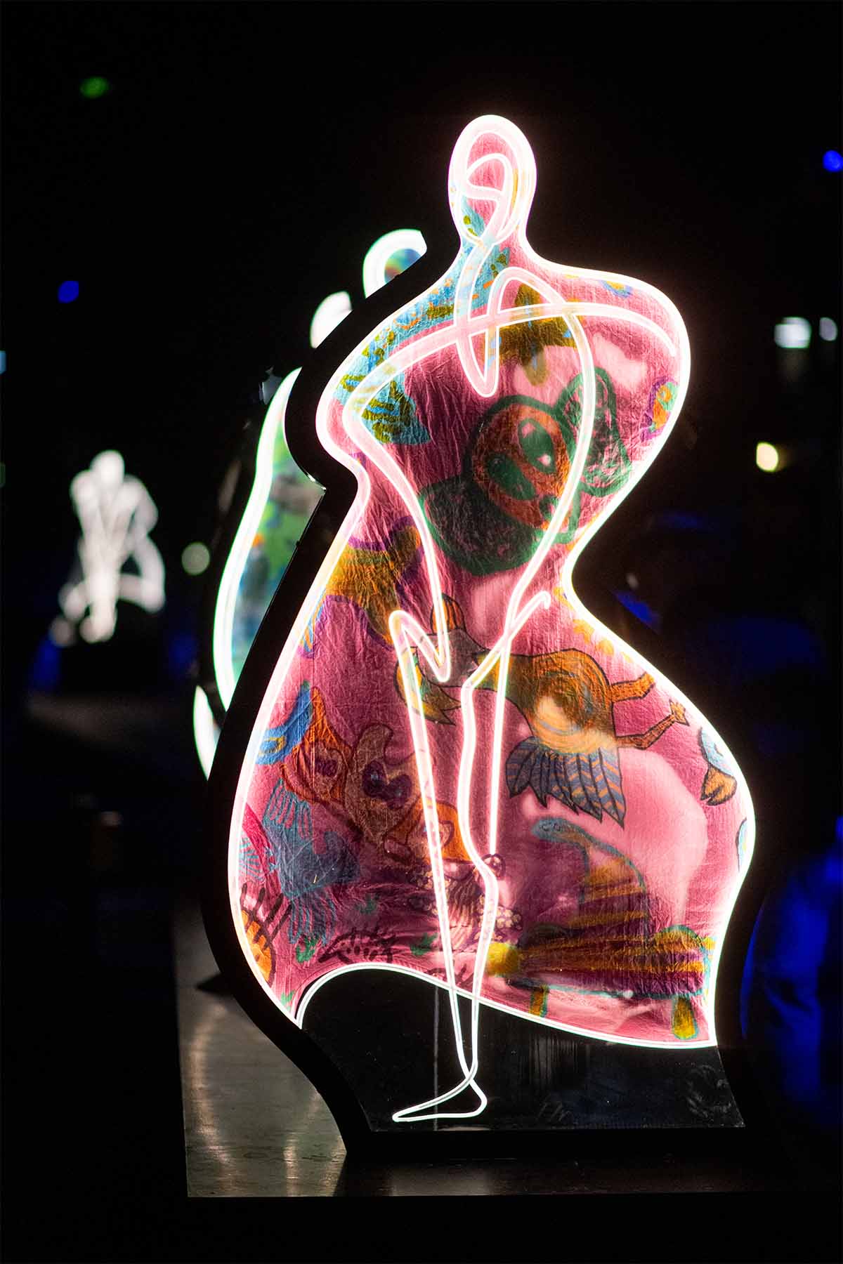 Brightly lit abstract sculpture with neon outlines and colorful, whimsical interior designs on a dark background.