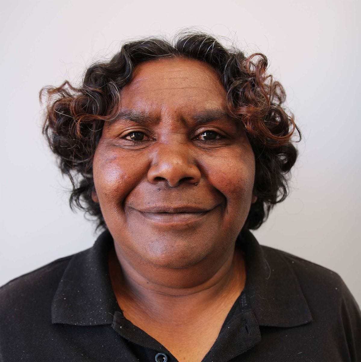 Smiling person with curly hair wearing a black shirt, set against a plain white background.
