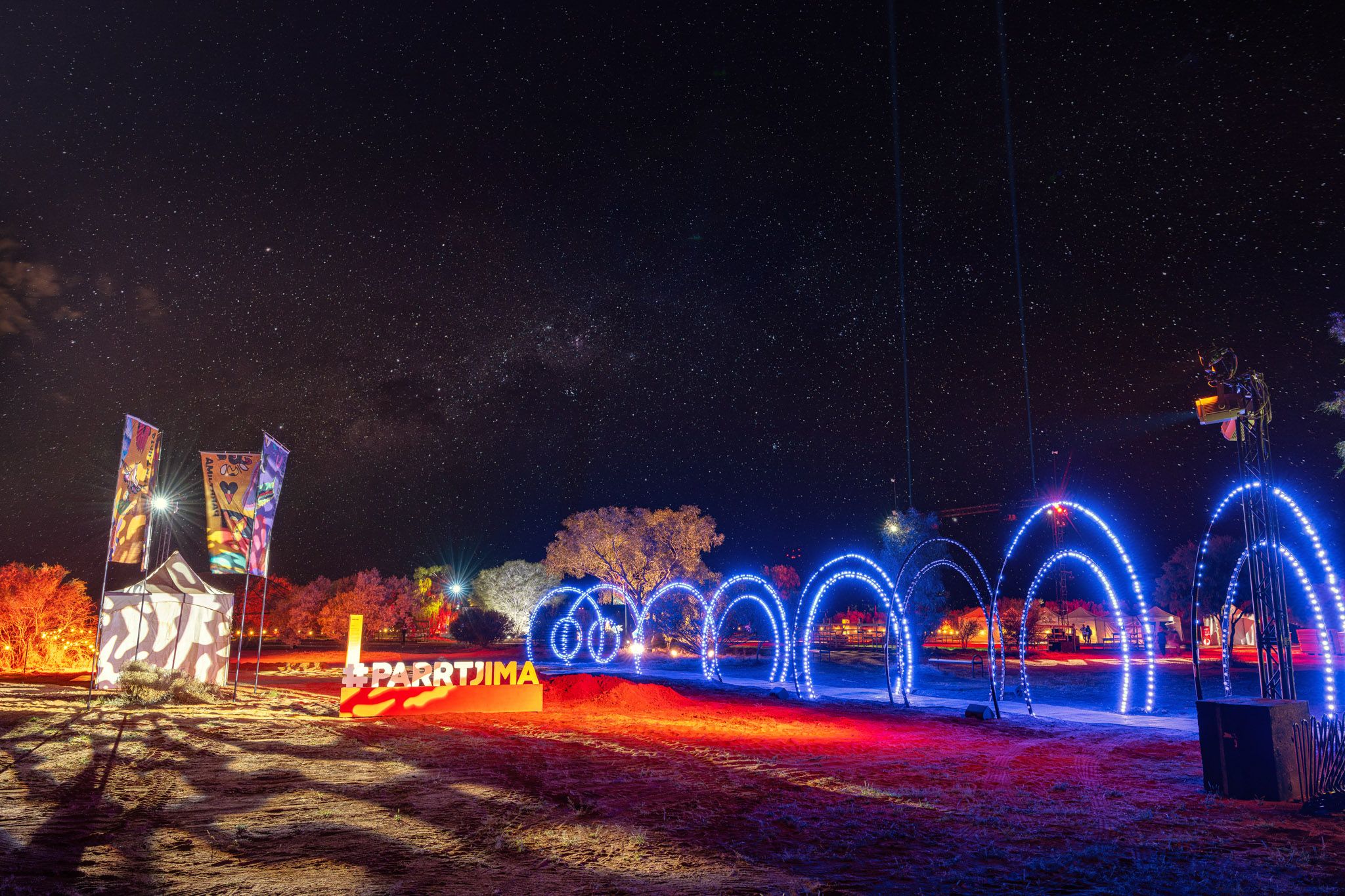 Nighttime outdoor light installation with illuminated arches and starry sky at Parrtjima festival.