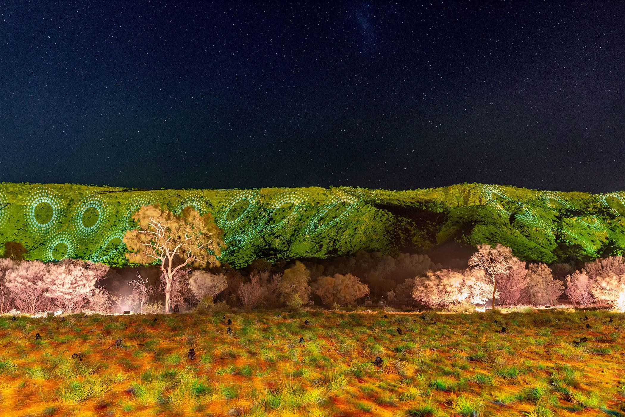 A starry night sky over green-lit hills with circle patterns and illuminated trees, creating a vibrant, mystical landscape.