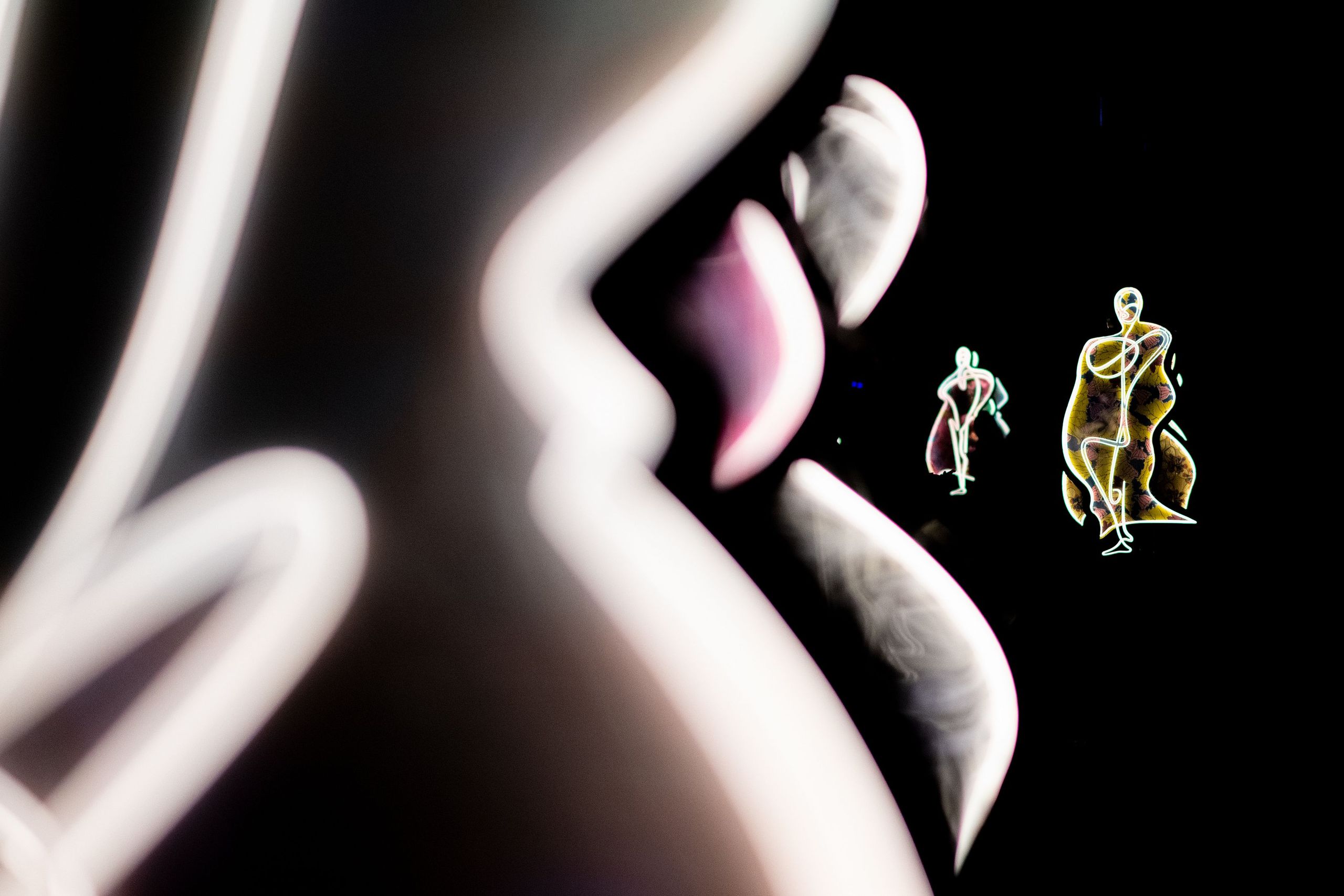 Abstract art featuring glowing, intertwined human figures and bold, curved shapes against a black background.